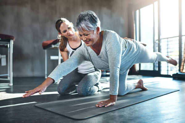 Working together to improve muscle strength and tone. Shot of a senior woman working out with her physiotherapist. Physical therapist helping smiling, gray haired woman with exercises on floor mat.