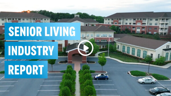 Outside view of senior living facility showing the parking lot, trees, and building in the background.