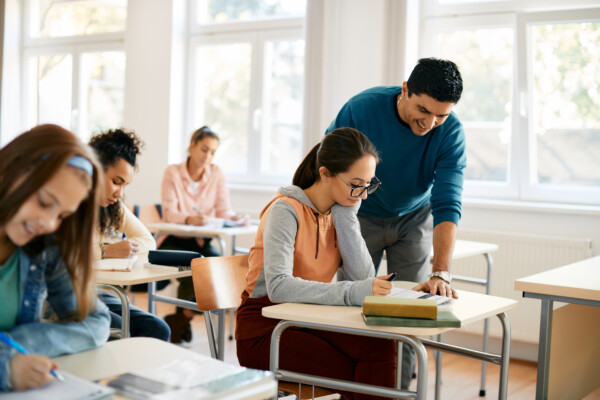 Female high school student learns with teacher’s help in classroom.