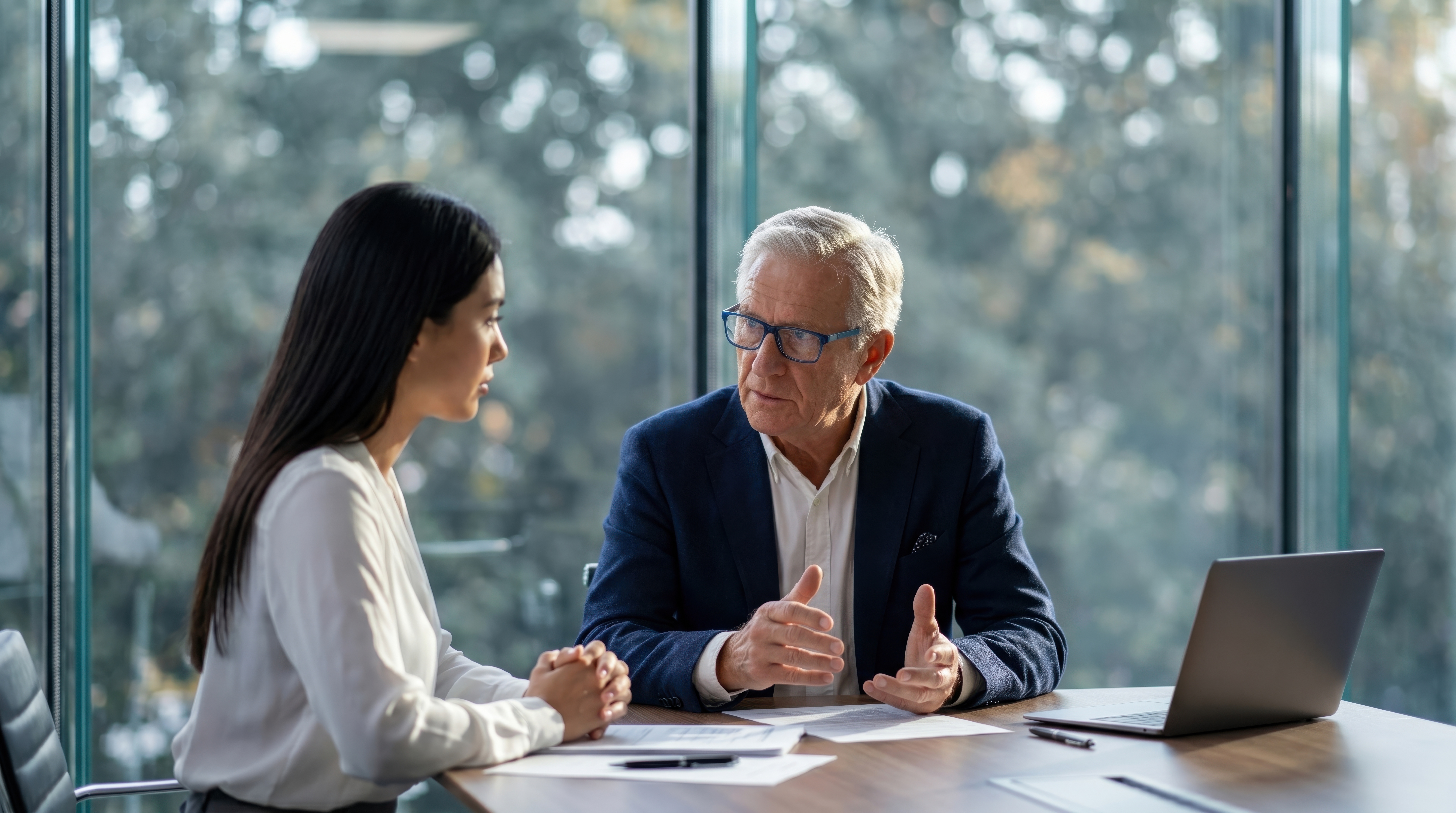 Two diverse business professionals engaged in serious discussion during a meeting in a modern office with large windows.